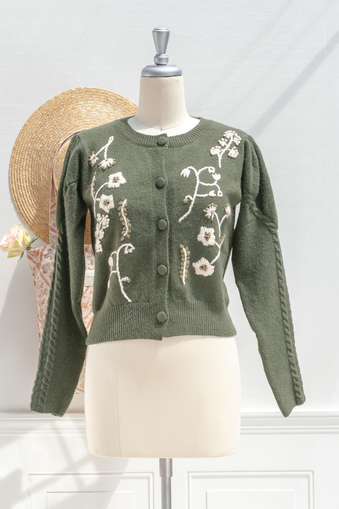Green knitted cardigan with floral embroidery on a mannequin against a white background