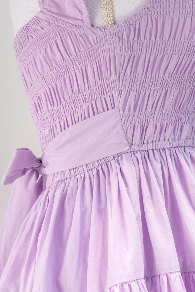 Sweet and feminine, the Lilac Meadows mini dress in lovely lavender cotton features a square neckline, short capped sleeves, fit-and-flare silhouette, and a smocked elastic bodice with side ties. fabric detail View