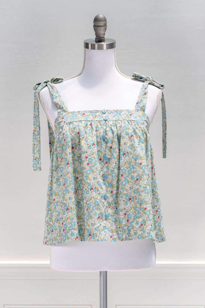The feminine aesthetic Watercolorist camisole features a blue and yellow floral print, tie-style shoulders, a button-up front, and a cute babydoll smock-style cut. amantine clothes - front view 