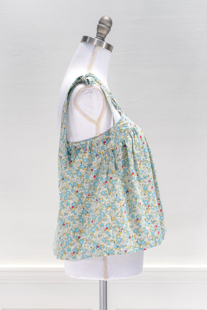 The feminine aesthetic Watercolorist camisole features a blue and yellow floral print, tie-style shoulders, a button-up front, and a cute babydoll smock-style cut. amantine clothes - side view 