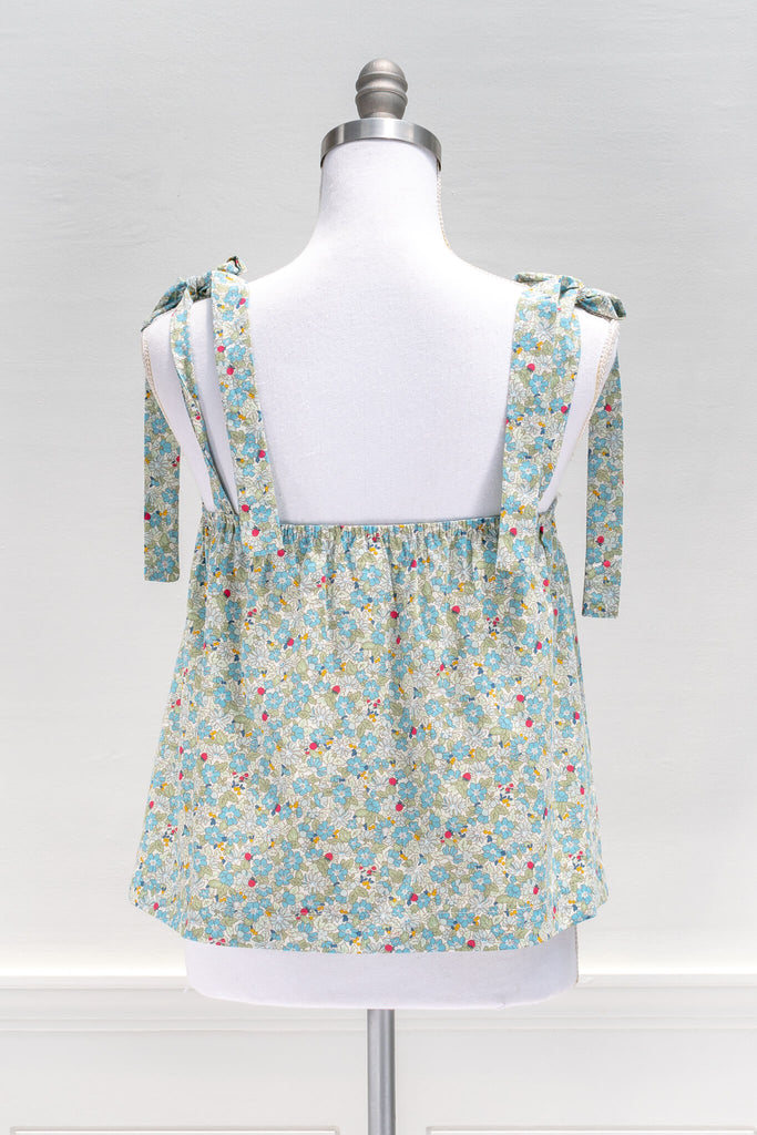 The feminine aesthetic Watercolorist camisole features a blue and yellow floral print, tie-style shoulders, a button-up front, and a cute babydoll smock-style cut. amantine clothes - back view 