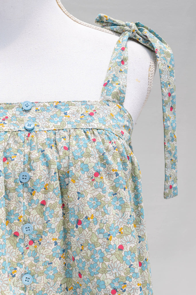 The feminine aesthetic Watercolorist camisole features a blue and yellow floral print, tie-style shoulders, a button-up front, and a cute babydoll smock-style cut. amantine clothes - fabric and button view 