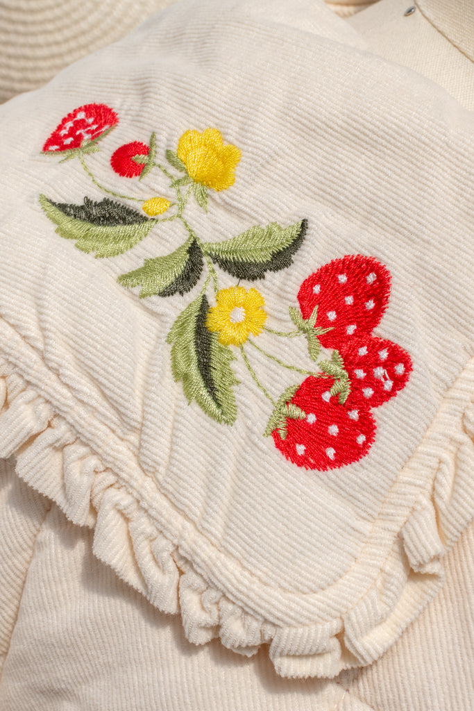 Close-up of strawberry and floral embroidery with ruffled edge on the Mari jacket collar