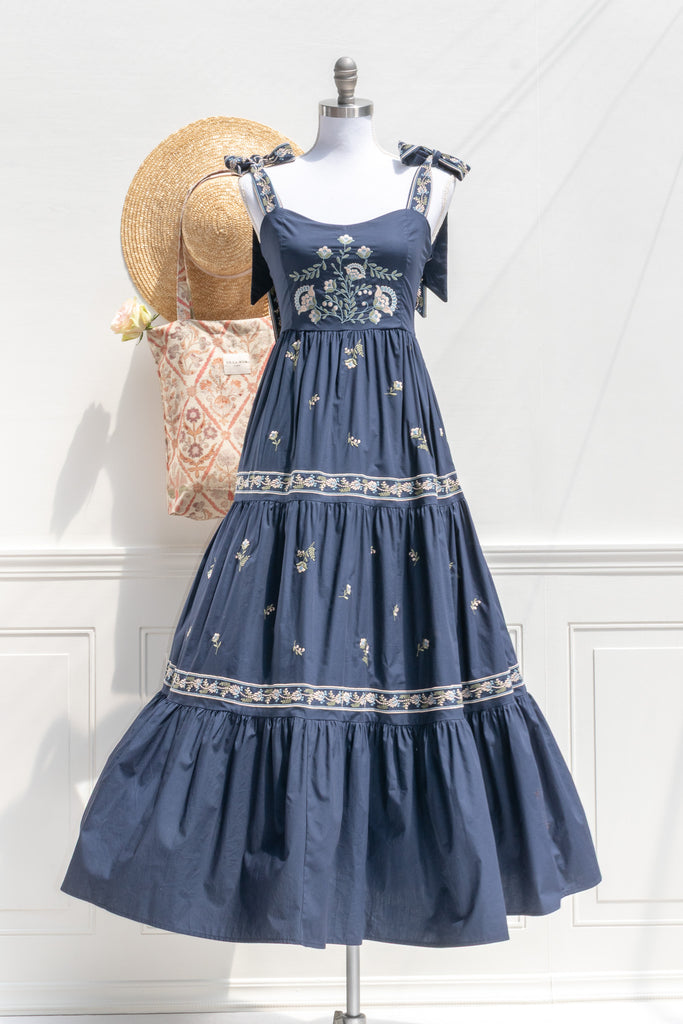 Blue floral dress on a mannequin with a straw hat and patterned bag against a white wall.