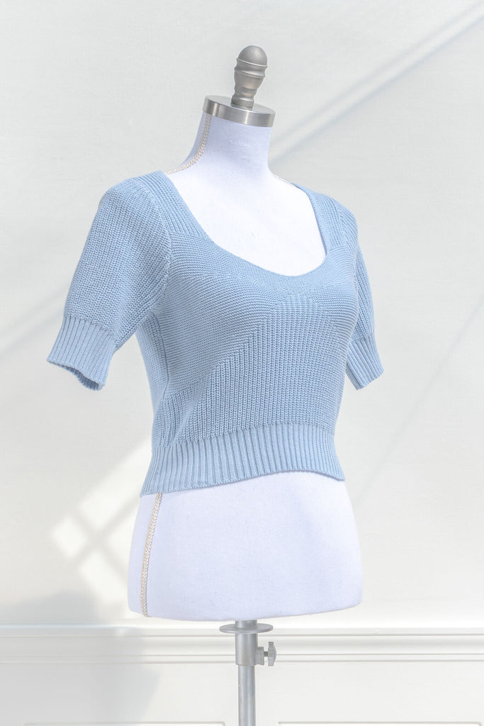 cottagecore outfits and feminine tops in french girl style. a blue knit top with short sleeves and low neckline. quarter side view. amantine. 