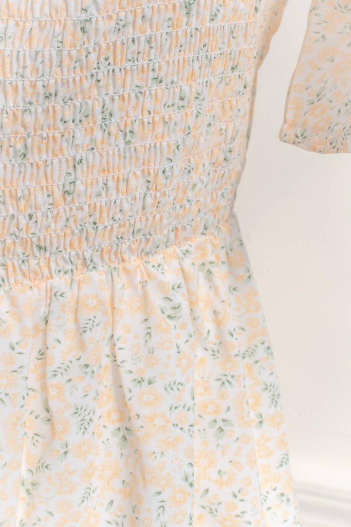 boutique dresses - a pretty mini dress with flutter sleeves, dresses with bows, and a v neckline. Yellow floral small print. cottagecore style. ruched fabric view. 
