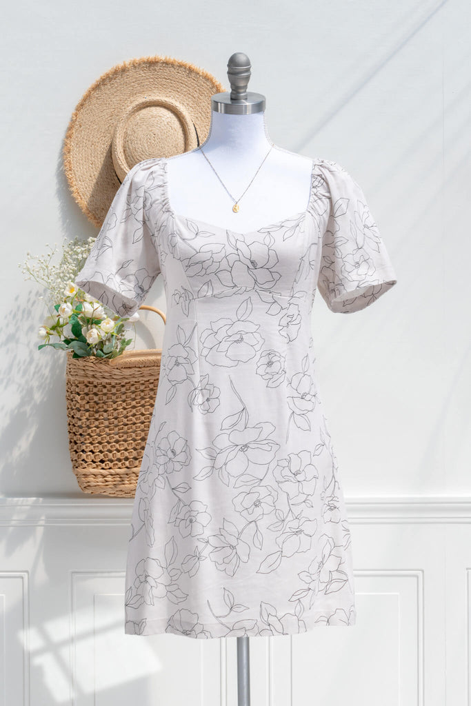 cottagecore dress - a mini dress with sweetheart neckline, short sleeves, side zipper, and graphic floral print on off white linen. front view, styled with sun hat and french woven tote. 