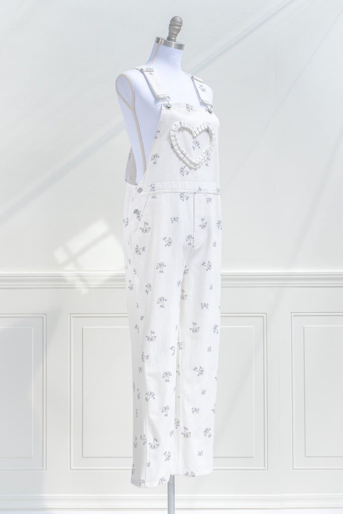 cottagecore outfits, a cottage core style jumpsuit, in white denim, small floral detail, and heart shaped applique detail. quarter side view. amantine.