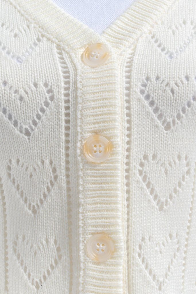 feminine tops - a french style cardigan sweater for spring. cream knit, button front, v neck, heart weave detail. up close knit fabric view. amantine. 