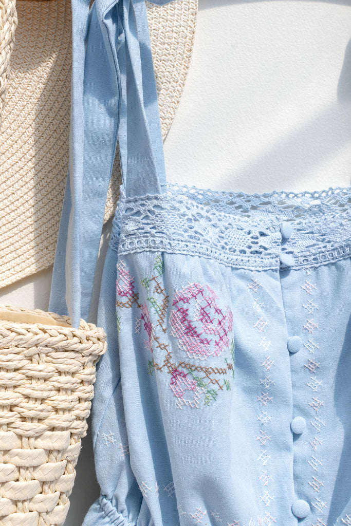 cottagecore style romper in periwinkle blue for spring time. with floral embroidery details and lace. fabric detail view. amantine. 
