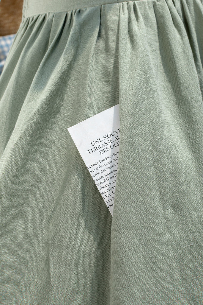 Green dress on a mannequin with a straw hat and bag in the background. French girl style dresses. 