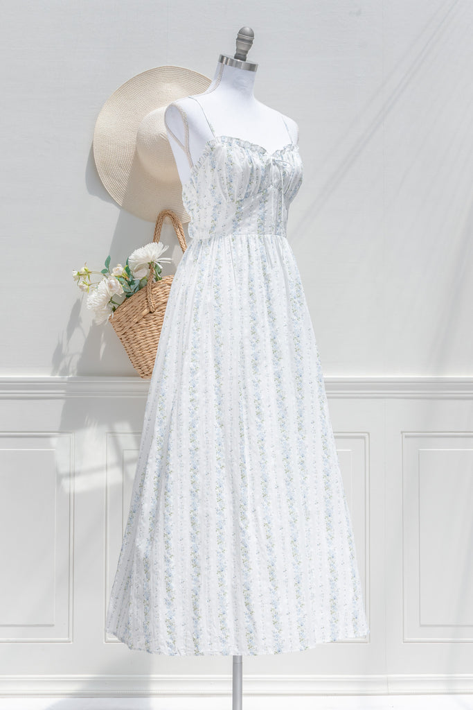 Floral cottagecore dress. Covered in soft vertical trails of blue and ivory florals, her silhouette feels like something from a countryside novel — soft, nostalgic, and effortlessly graceful. 3/4 side view. Amantine french style.