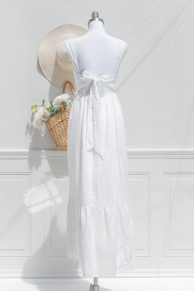 A dress made for summer promenades, the Sophie Maxi in white 100% cotton features romantic eyelet lace fabric, a higher waistline for a regency-inspired silhouette, a flattering square neckline, adjustable shoulder straps with ruffled details, and an open back with a bow. back  View. amantine. 
