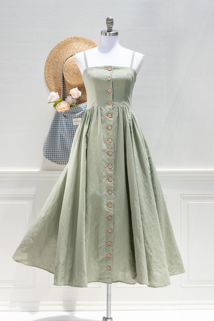 Green dress on a mannequin with a straw hat and bag in the background. French girl style dresses. 