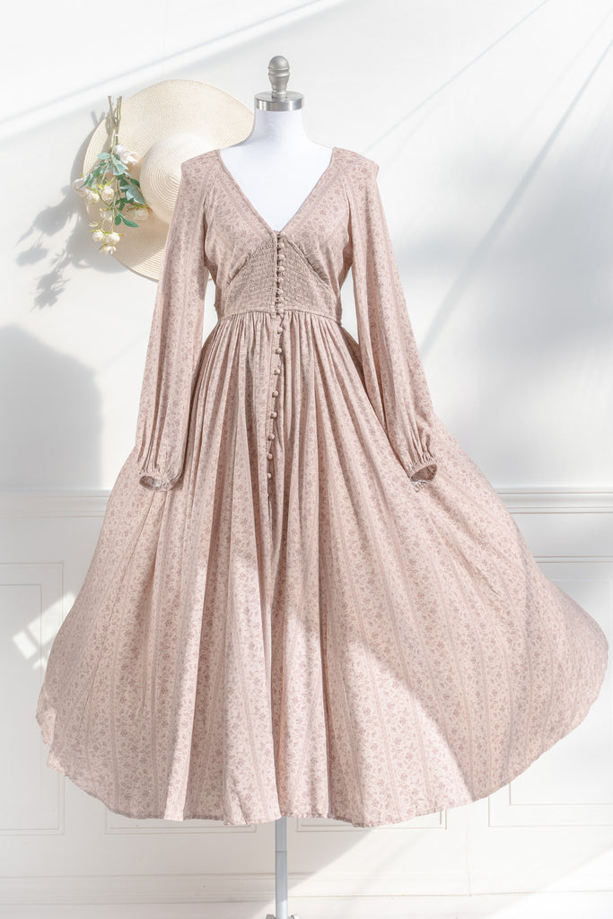 long sleeve modest cottagecore dress. small floral detail on beige  background. button down and ruched midriff. cottagecore style dresses with a french twist. front view. 