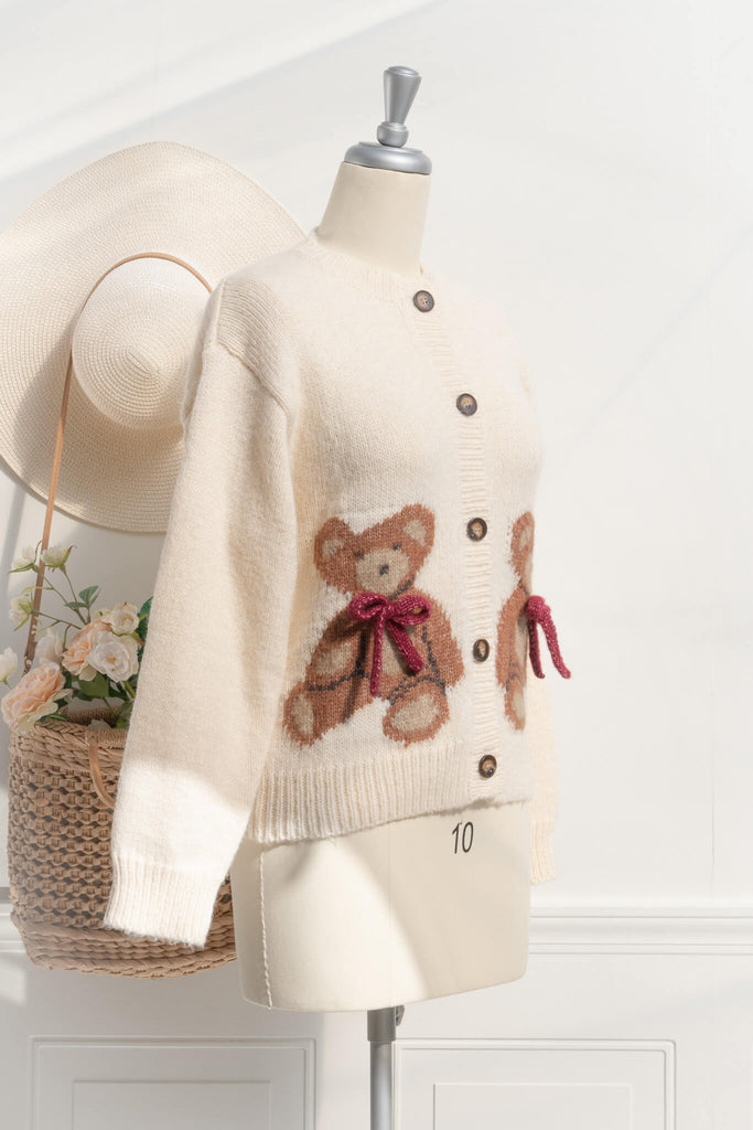 a cute sweater with a crew neckline, long sleeves, button down closure, and a teddy bear print with a 3d bow detail. Front view. amantine. 