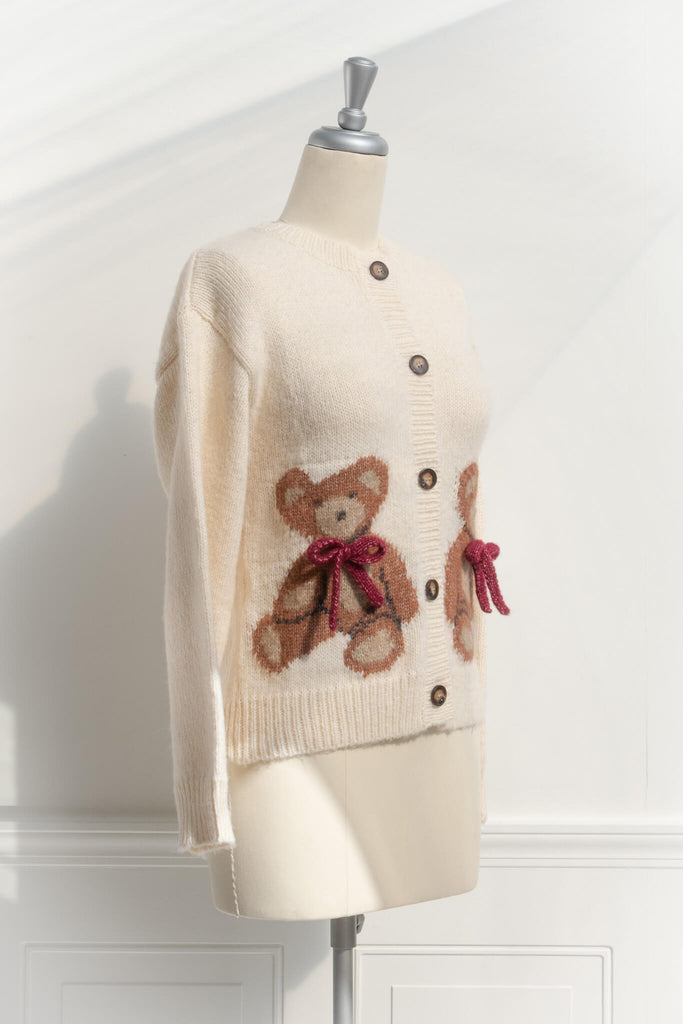 a cute sweater with a crew neckline, long sleeves, button down closure, and a teddy bear print with a 3d bow detail. side view. amantine. 