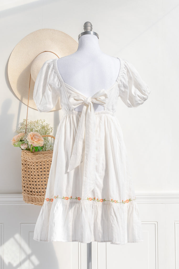 back view of white cottagecore dress with orange floral embroidery featuring a square neckline puff sleeves and a delicate bow closure for a romantic look.
