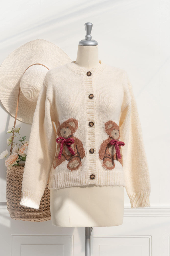 a cute sweater with a crew neckline, long sleeves, button down closure, and a teddy bear print with a 3d bow detail. Front view. amantine. 