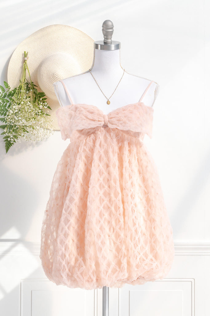 bow dress - a feminine dress with a bow in the front in pink and textured organza. Amantine. styled with a feminine hat and flowers View. 