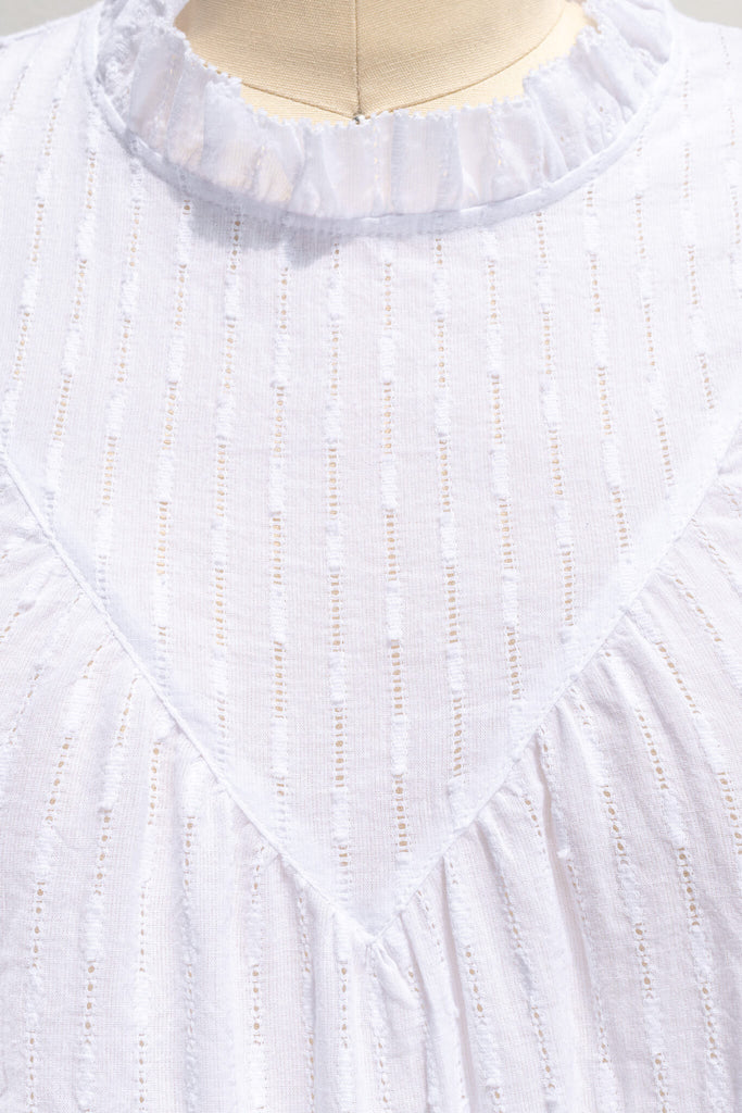 feminine tops - a cottagecore style white blouse with a ruffled crew neckline, ruffled sleeves, and white fabric. fabric upclose view. 
