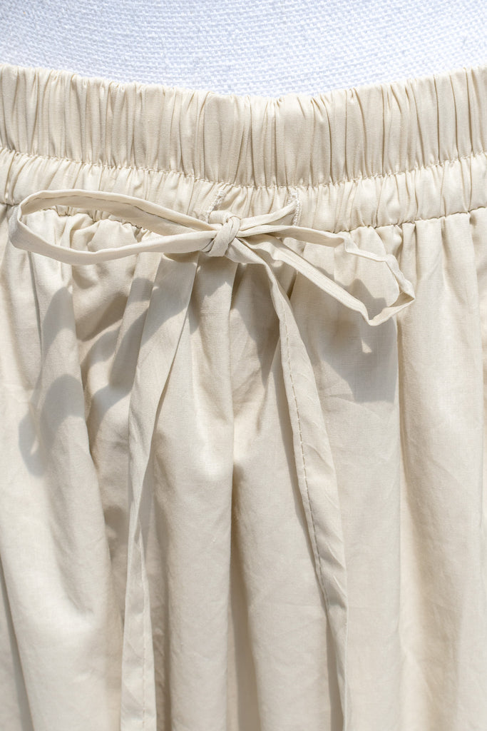Close-up of beige skirt with an elastic waistband and drawstring on a light blue background.