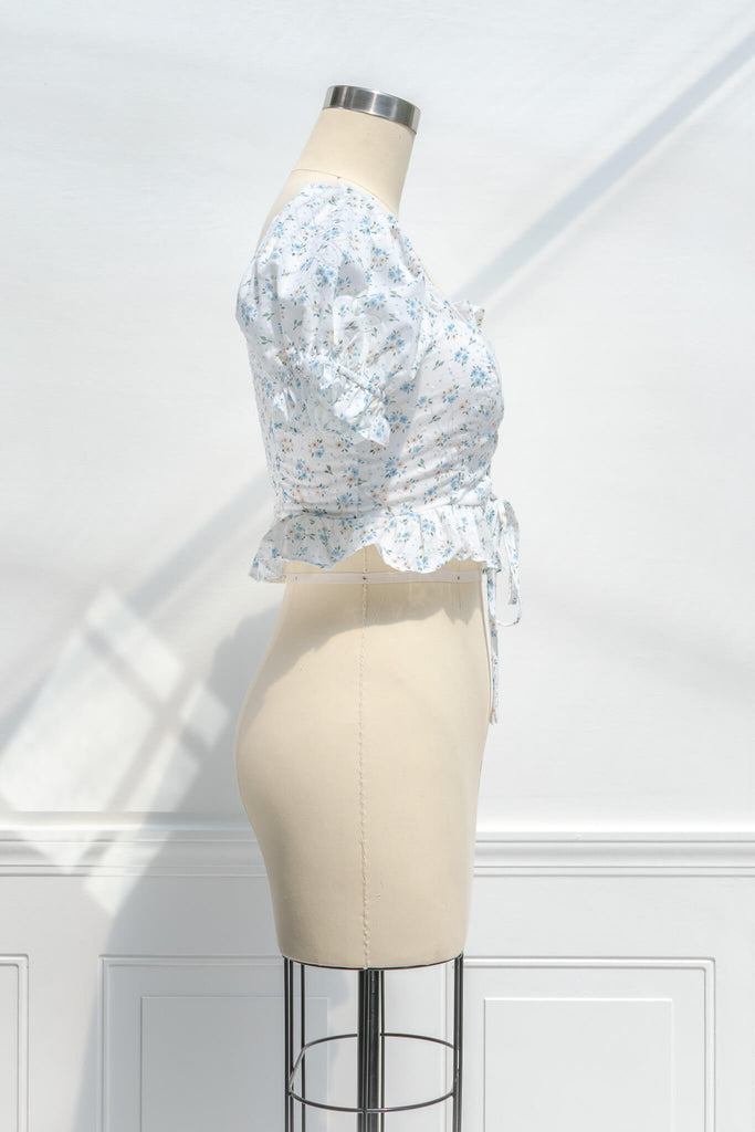 feminine clothing - photo shows a feminine blouse, with a square neckline, puff sleeves, ruffled waist, and cropped lenght with a light blue on white floral print - side view. 