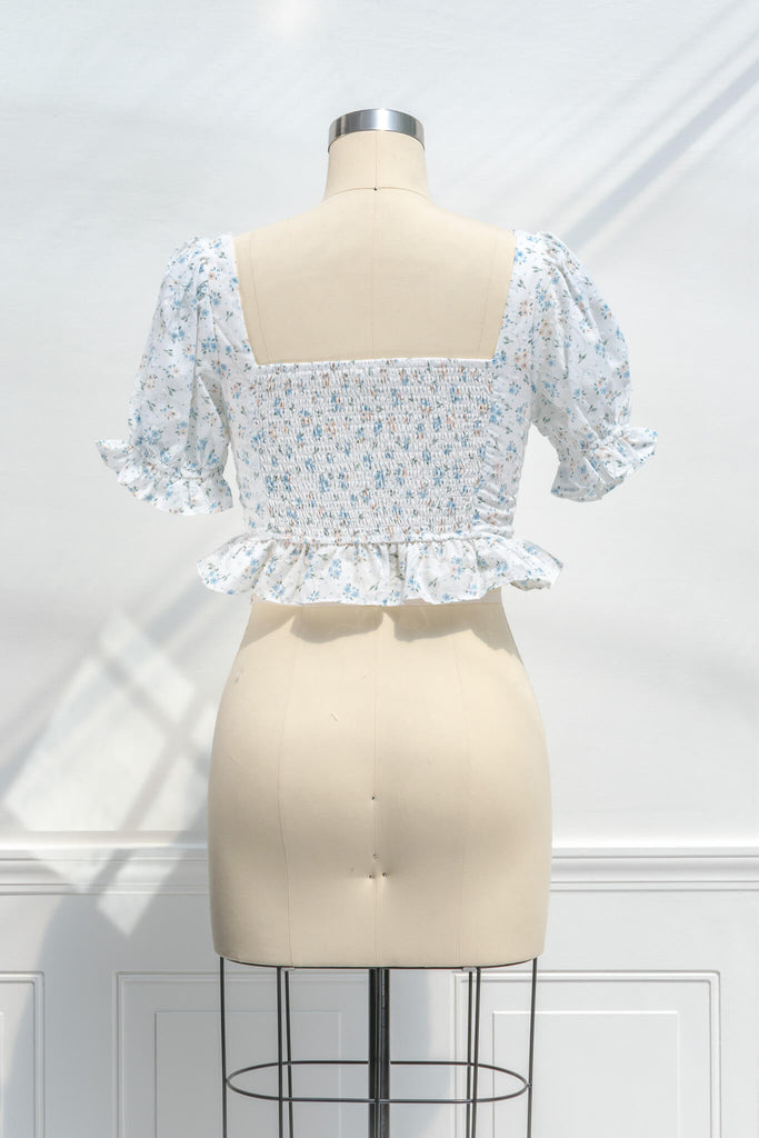feminine clothing - photo shows a feminine blouse, with a square neckline, puff sleeves, ruffled waist, and cropped lenght with a light blue on white floral print - back view. 