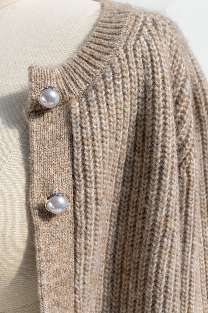 A cozy and comfy cardigan for autumn, the Isobel sweater features faux-pearl buttons, cropped length, a crew neckline, and long sleeves in a soft taupe knit. fabric view. 