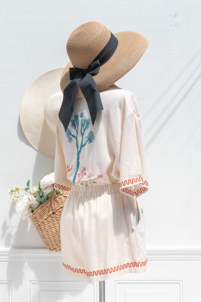 feminine clothing - a very unique summer set featuring a short sleeve button down shirt and shorts. In cream linen blend, it features very cute embroidery including a horse, and florals. A beautiful choice for your summer getaways. Front view styled with sun hat and french tote. amantine french style clothing. 