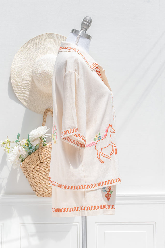 feminine clothing - a very unique summer set featuring a short sleeve button down shirt and shorts. In cream linen blend, it features very cute embroidery including a horse, and florals. A beautiful choice for your summer beach getaways. side view. amantine french style clothing. 