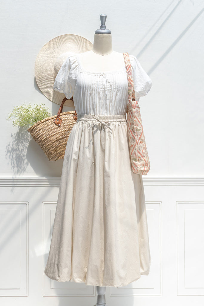 Mannequin wearing a white top and beige skirt with a straw bag and hat on a white background