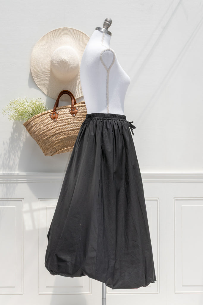french girl style Black skirt on a mannequin with a straw bag and hat against a white wall