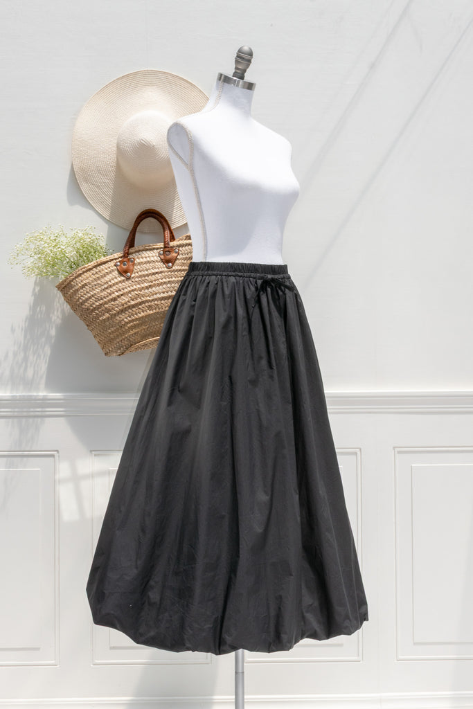 Black skirt on a mannequin with a straw bag and hat against a white wall