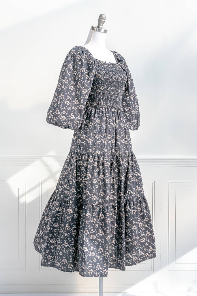 french dresses - dress with a smocked bodice, open-tie back, 3/4 length puffed sleeves, and a delicate vintage style taupe floral print on black. quarter view. Amantine. 