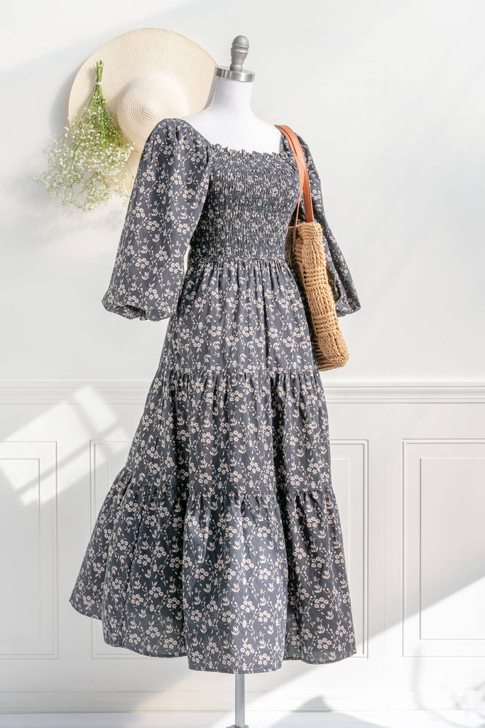 french dresses - dress with a smocked bodice, open-tie back, 3/4 length puffed sleeves, and a delicate vintage style taupe floral print on black. styled with a french tote bag view. Amantine. 