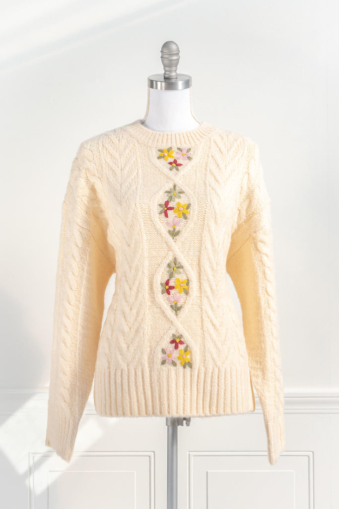 cottage core and feminine tops. an oversized knit style, long sleeves, cable-knit, and lovely embroidered florals in a cream fabric. front view. amantine. 