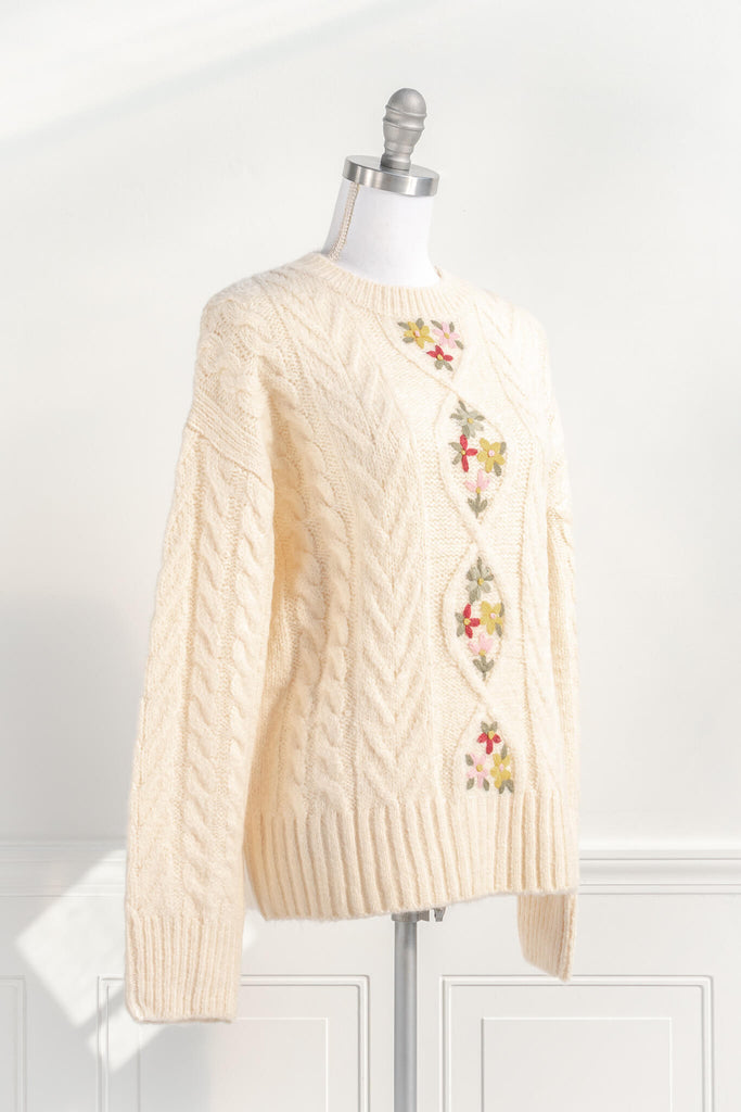 cottage core and feminine tops. an oversized knit style, long sleeves, cable-knit, and lovely embroidered florals in a cream fabric. quarter view. amantine. 