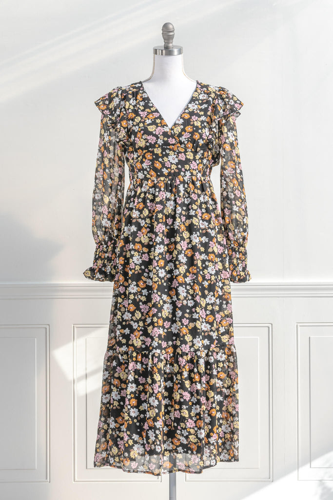 cottagecore and cottage core dresses in a vintage and french style cut. a v neck, long sleeve, midi floral dress. it features a black chiffon with yellow, white, and orange little flowers throughout. front view. amantine cottagecore dresses.