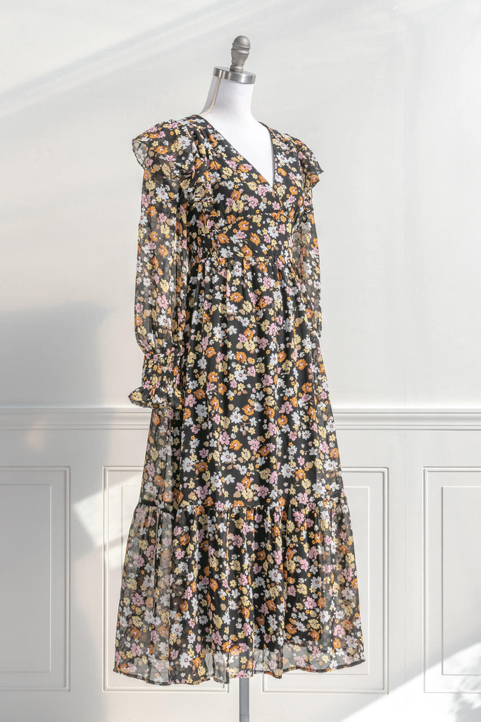 cottagecore and cottage core dresses in a vintage and french style cut. a v neck, long sleeve, midi floral dress. it features a black chiffon with yellow, white, and orange little flowers throughout. front view. amantine cottagecore dresses.