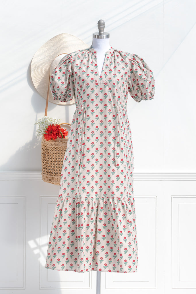 french dresses - a cottagecore style french girl dress in cotton, featuring a taupe fabric with stylized red and green florals. puff sleeves, v neck, drawstring waist and a line silhouette. front view showing untied front detail. 