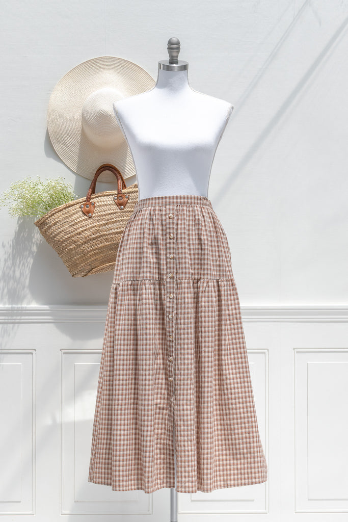 Mannequin wearing a checkered skirt with a straw bag against a white wall. French girl aesthetic for autumn. 