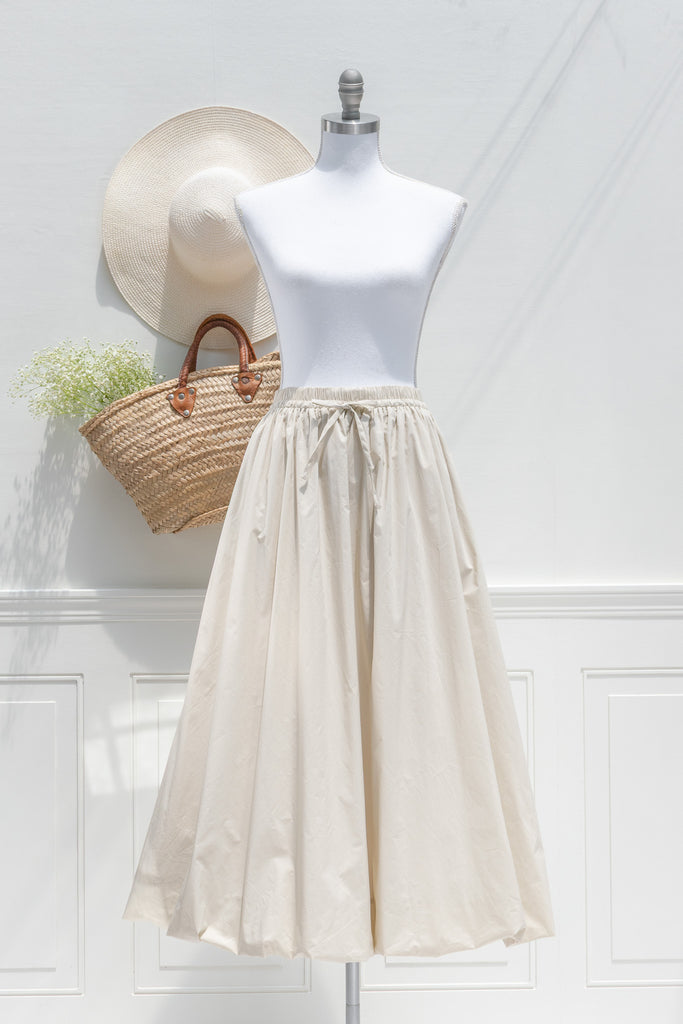 Mannequin wearing a beige skirt with a straw bag and hat on a white background