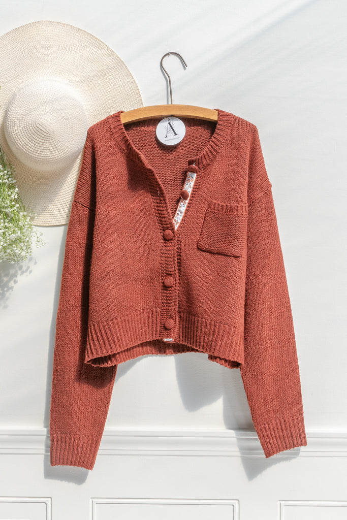 french tops. feminine cottagecore style. a cute rust color button down cardigan. shown on hanger. amantine. 