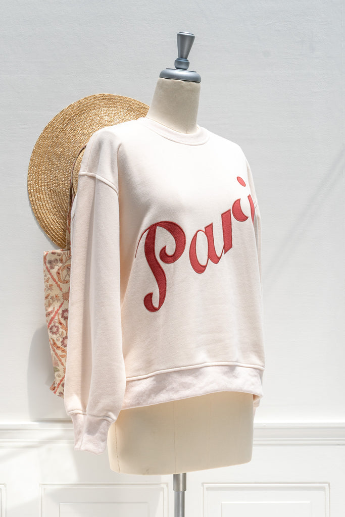 White sweatshirt with 'Paris' printed in red on a mannequin against a white wall.