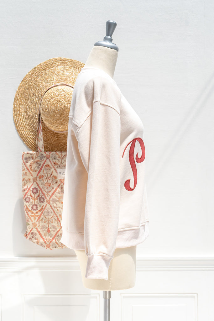 Mannequin wearing a white sweatshirt with a red logo, straw hat, and patterned bag on a white background