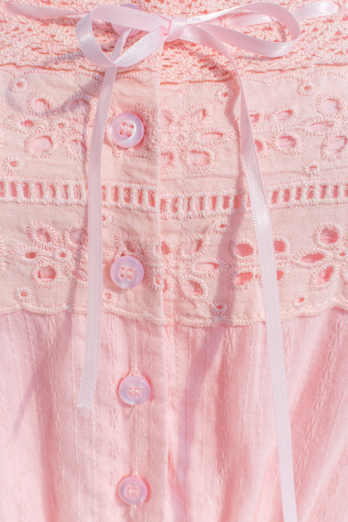 Close-up of pink dress fabric highlighting intricate lace patterns and soft pink material.