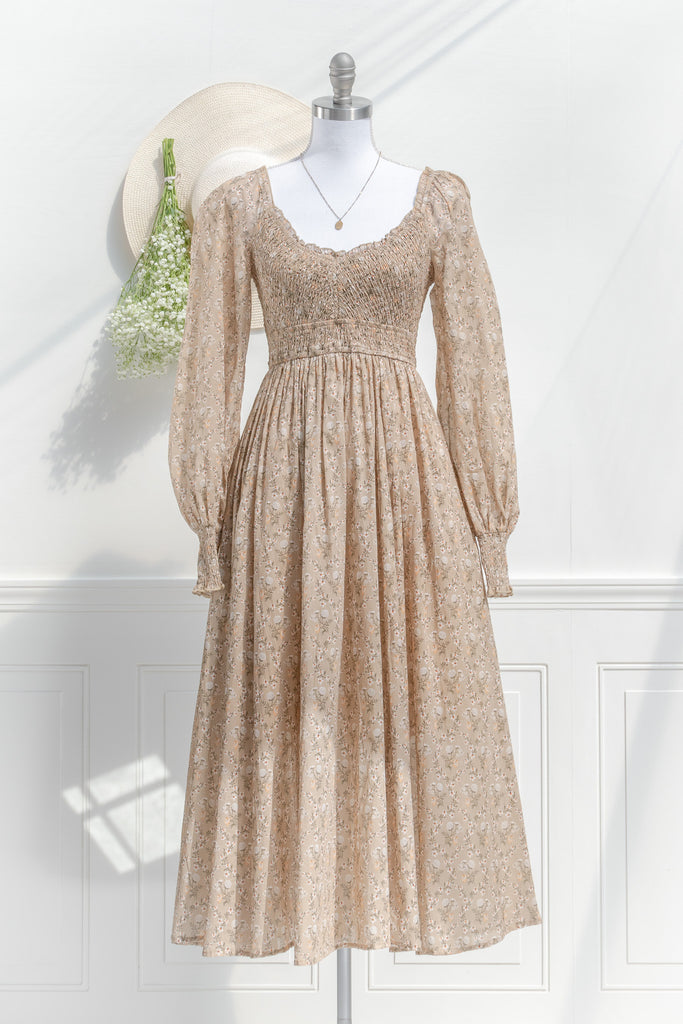 prairie dress in a fall fashion style. round neckline, long sleeves, smocked bodice, long skirt. Taupe brown cotton fabric with floral details in in cream and brown. front view. amantine 