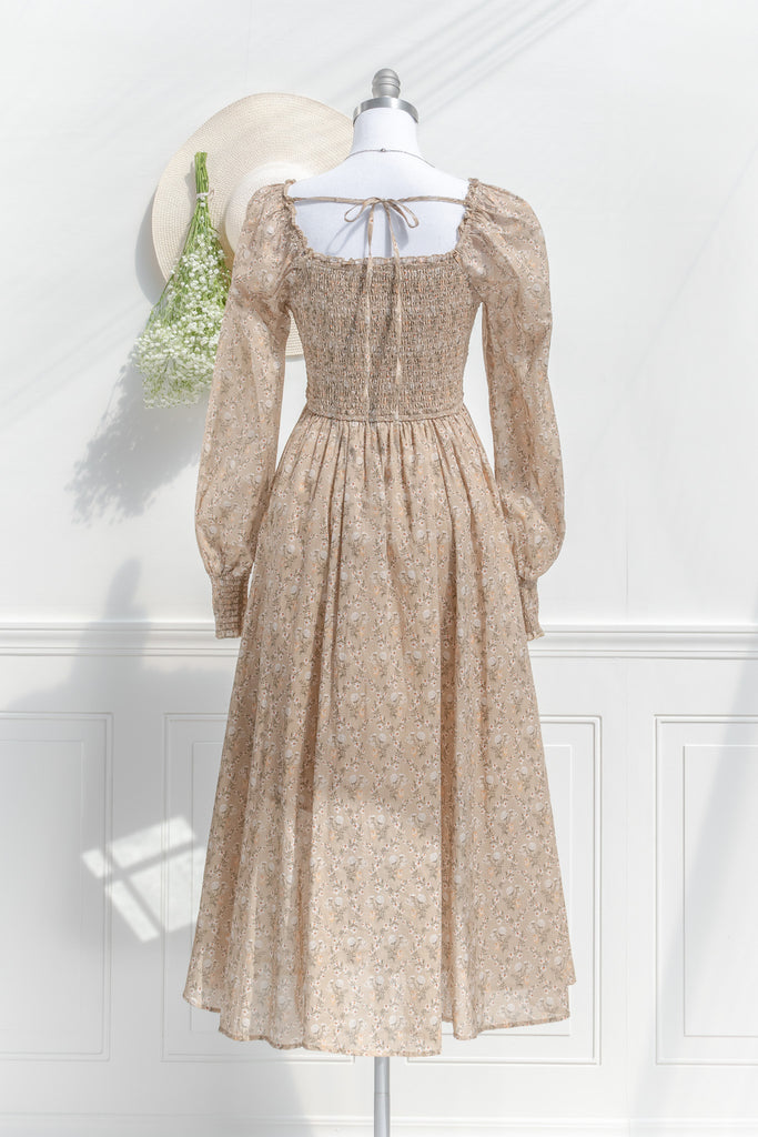 prairie dress in a fall fashion style. round neckline, long sleeves, smocked bodice, long skirt. Taupe brown cotton fabric with floral details in in cream and brown. back view. amantine 