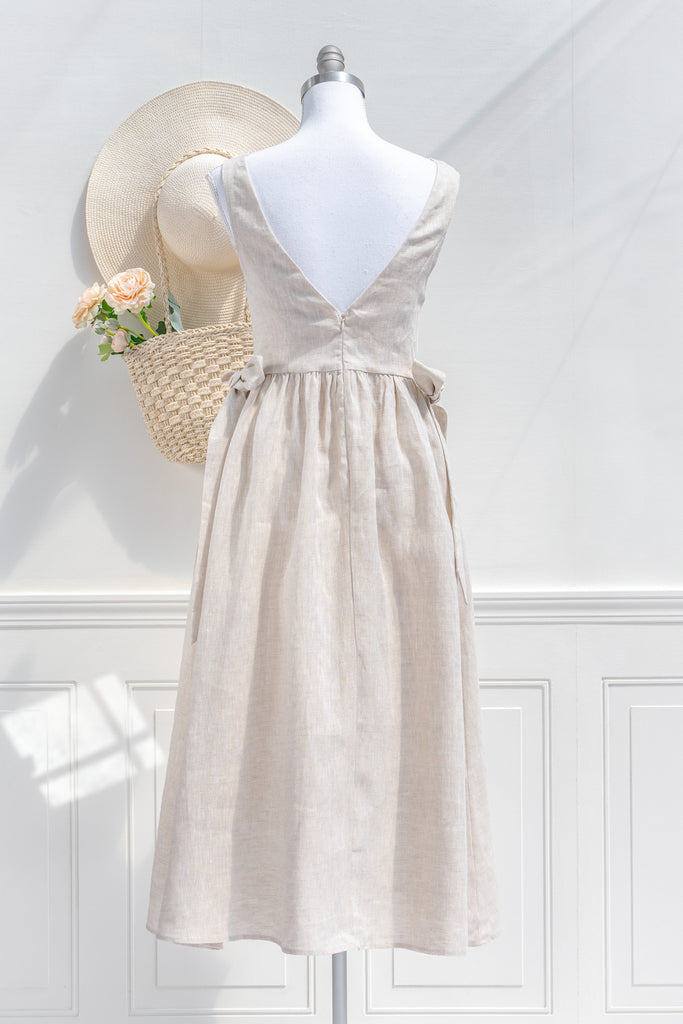 pretty dresses. cottagecore dress in beige linen. v neckline, side bows, side pockets, perfect for spring time daytime outfits. back view. 